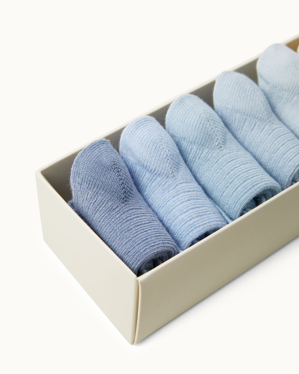 Close-up of Bijou socks set showing ribbed texture and varying blue shades rolled in an ivory box