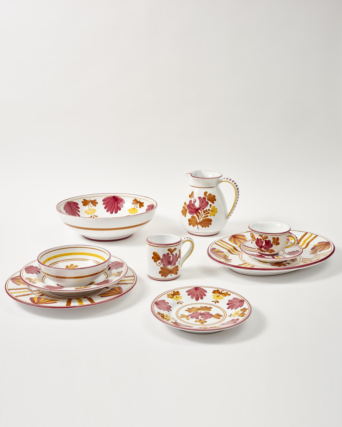 Blossom Mug, Yellow showcasing hand-painted burgundy and yellow floral pattern among matching tableware on a white background