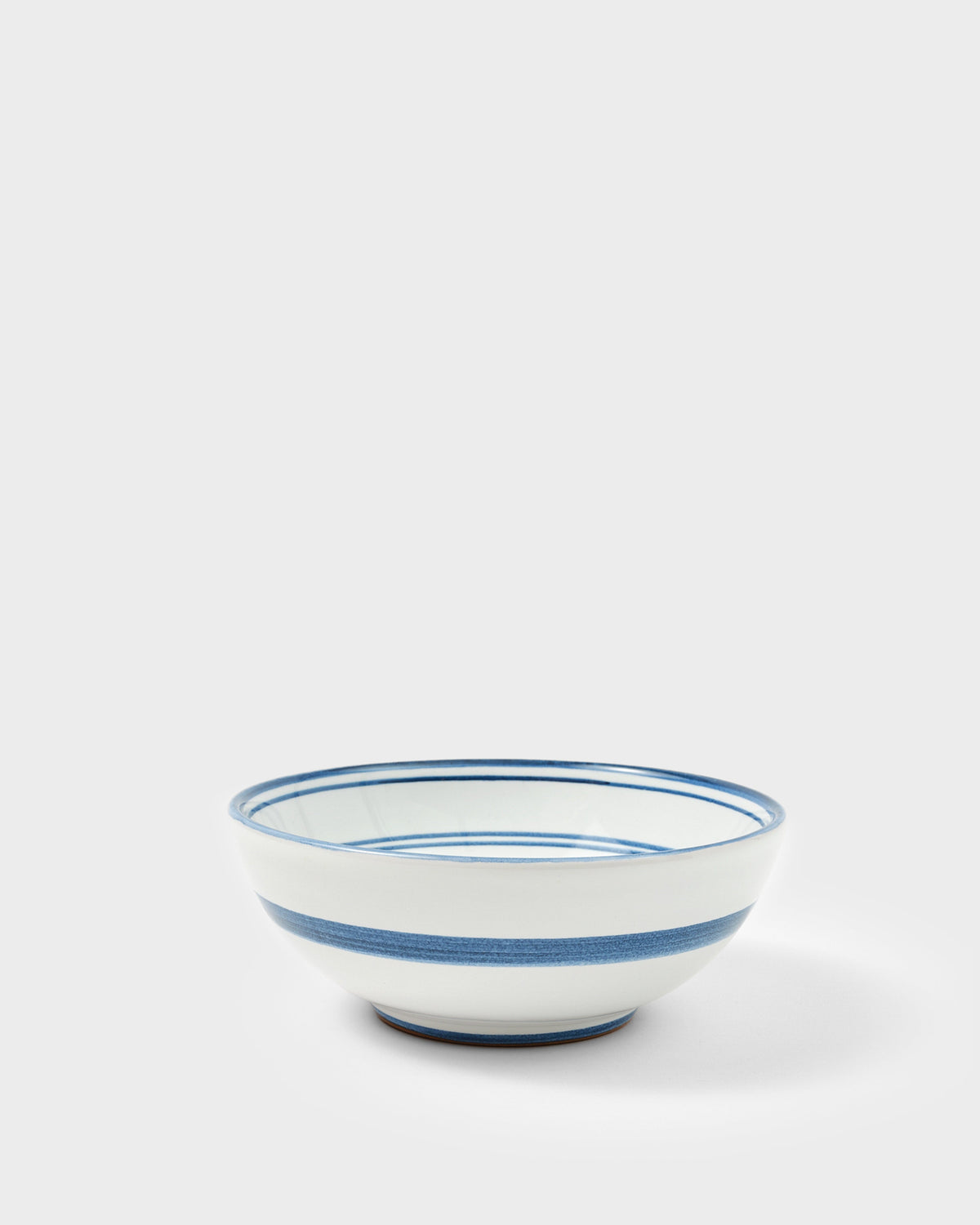 Three-quarter view of Blossom Bowl in midnight blue showing hand-painted blue bands on white ceramic on a light gray background