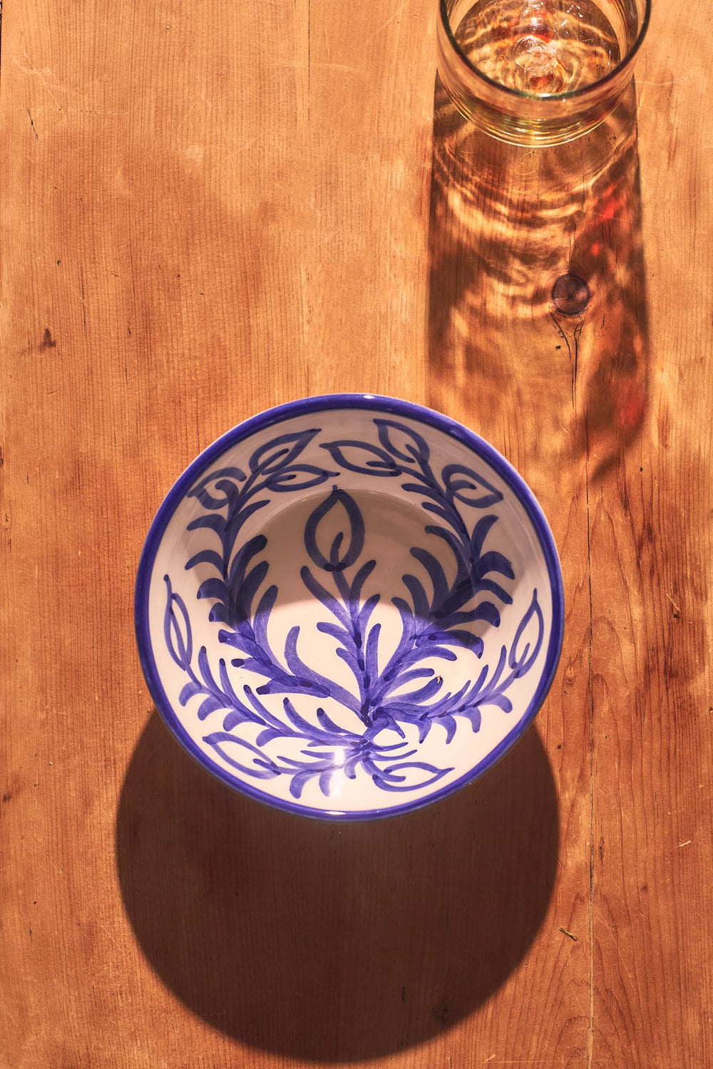 Overhead view of Blue Vina Bowl showing hand-painted blue floral Vina pattern on white ceramic on a wooden table with a glass shadow