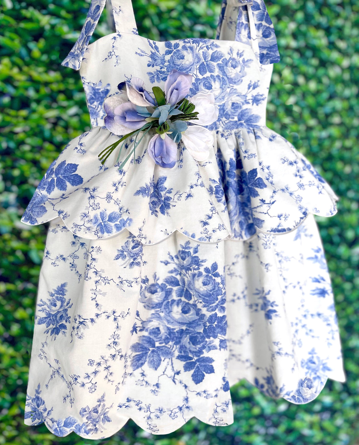 Front view of Scallop Peplum Petal Dress in Blue Toile de Jouy with scalloped hem, shoulder bows, and waist flower pin