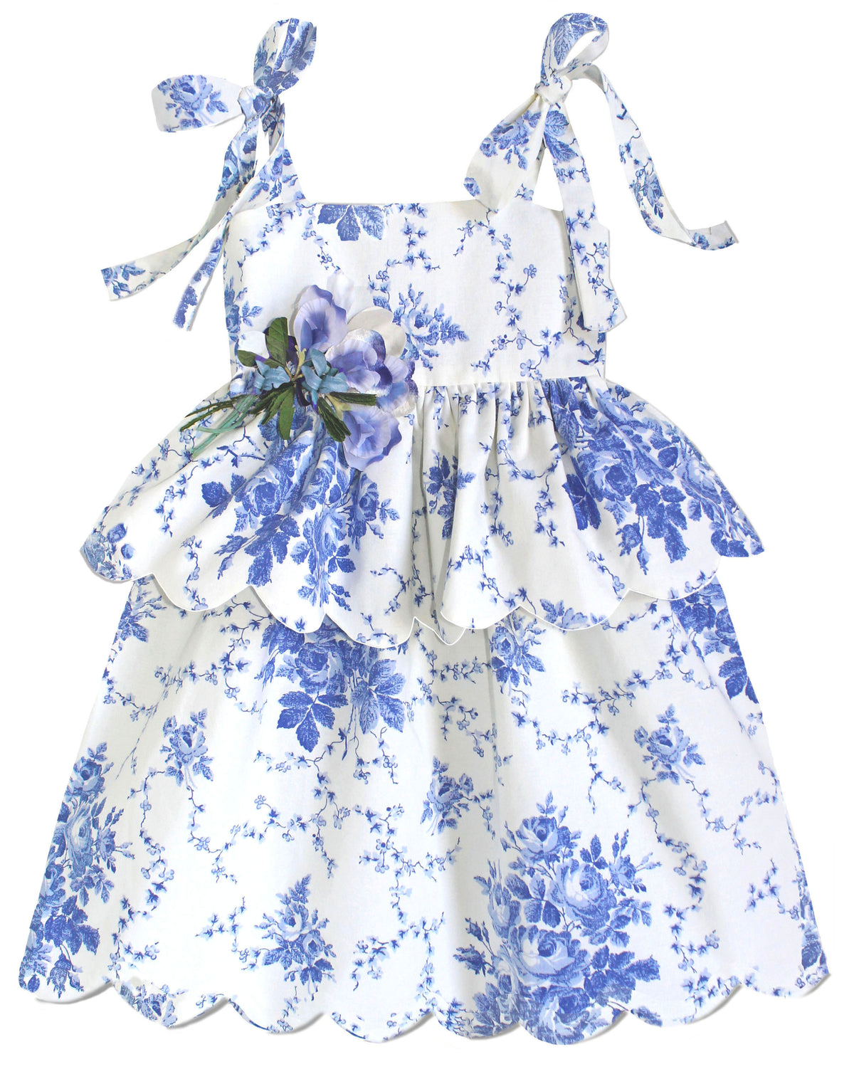 Front view of Scallop Peplum Petal Dress in Blue Toile de Jouy with shoulder bows, waist flower, and scalloped hem on white