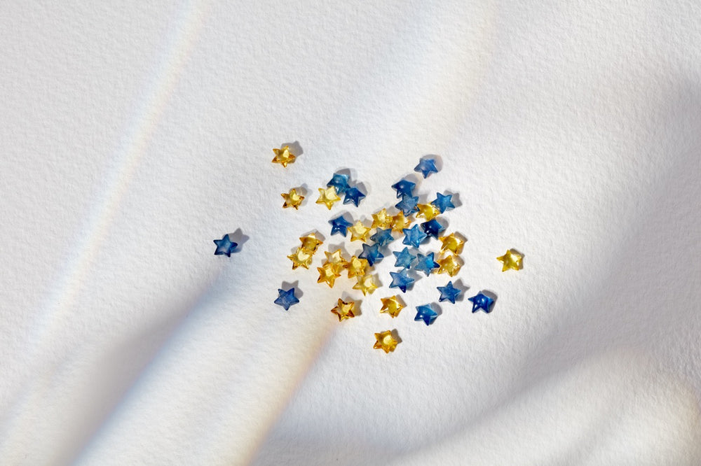 Close-up of Blue Sapphire star charms showcasing small faceted blue and yellow stars on white textured fabric