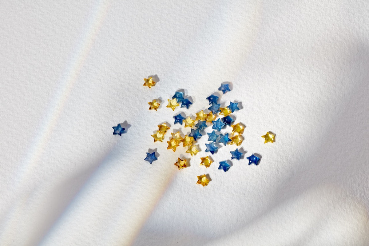 Close-up of Blue Sapphire star charms showcasing small faceted blue and yellow stars on white textured fabric