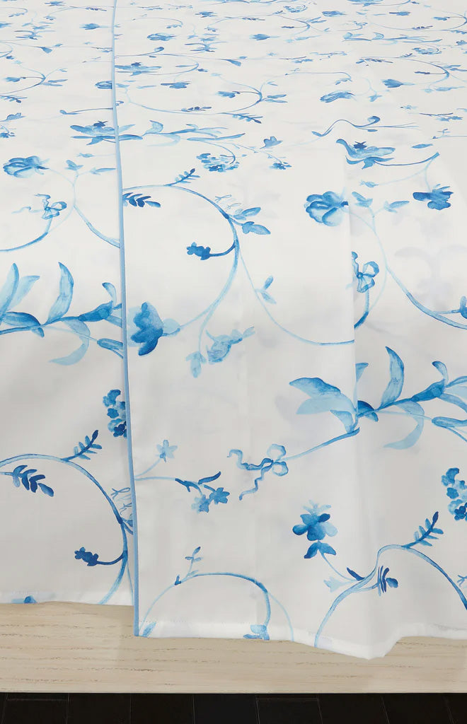 Close-up of Botanical top sheet showing blue watercolor floral print on white brushed cotton sateen draped over a light wood bed edge