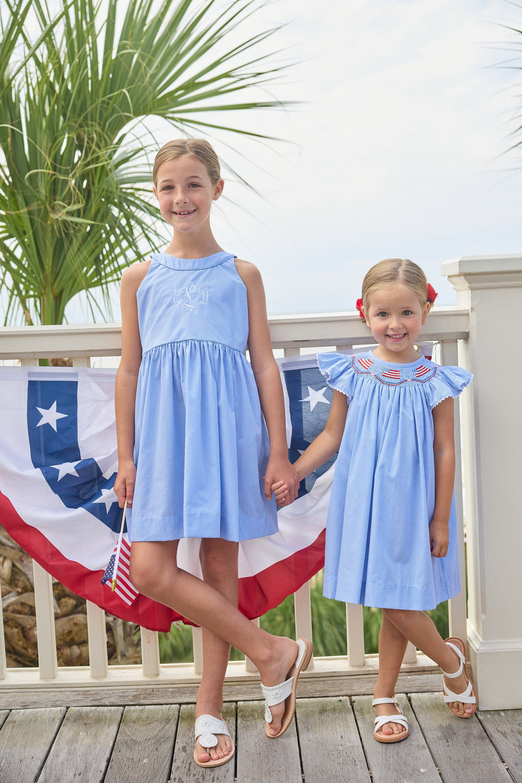 Little English traditional children's clothing. Flutter sleeve dress for toddler girls in royal blue mini gingham with smocking at the collar and American flag bunting