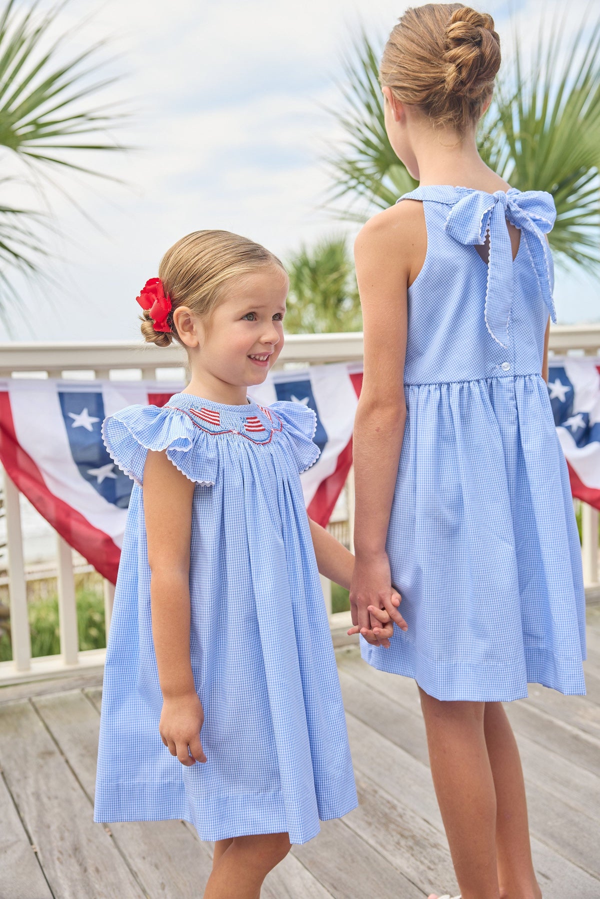 Little English traditional children's clothing. Flutter sleeve dress for toddler girls in royal blue mini gingham with smocking at the collar and American flag bunting