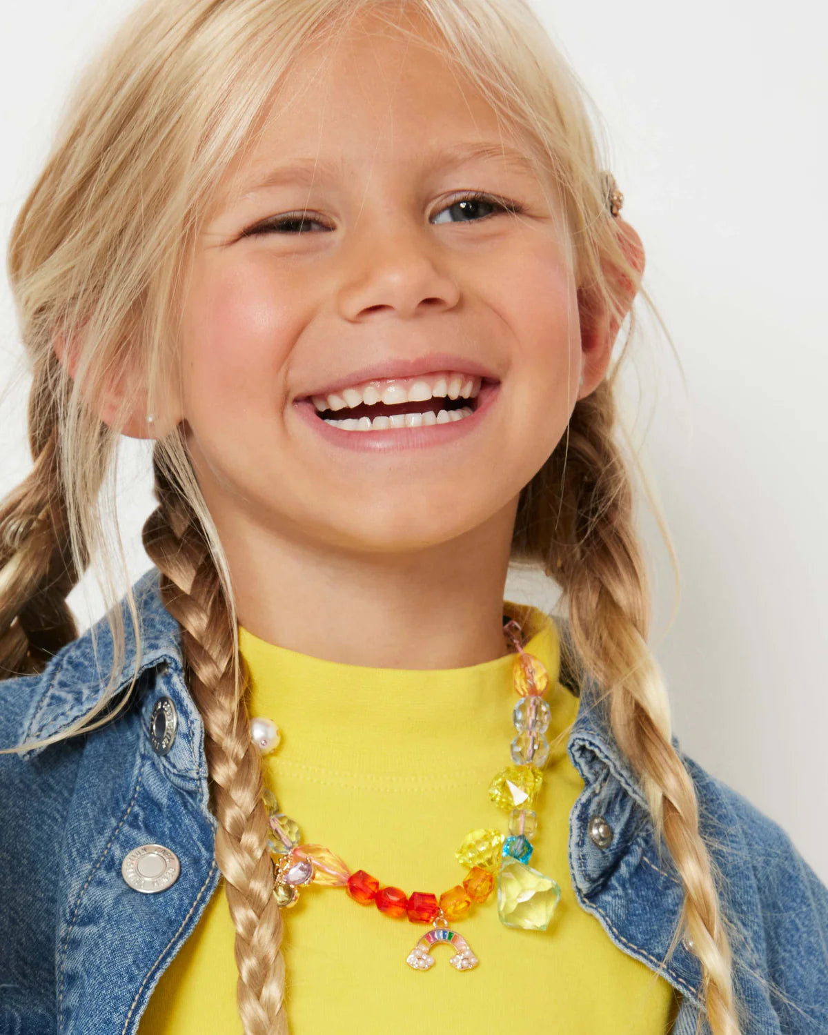Close-up of Make It Rainbow Mini Bead Kit showcasing colorful beads and rainbow charm on a smiling child
