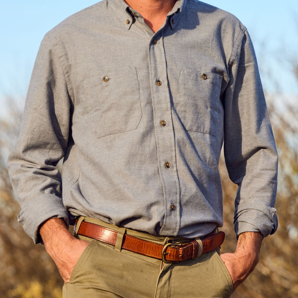 Man wears Tom Beckbe Dixon Brushed Cotton Twill Shirt with khaki pants and brown belt, hands in pockets outdoors.