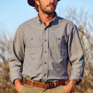 Man wearing a Tom Beckbe Dixon Brushed Cotton Twill Shirt, brown belt, and hat outdoors with trees in the background.