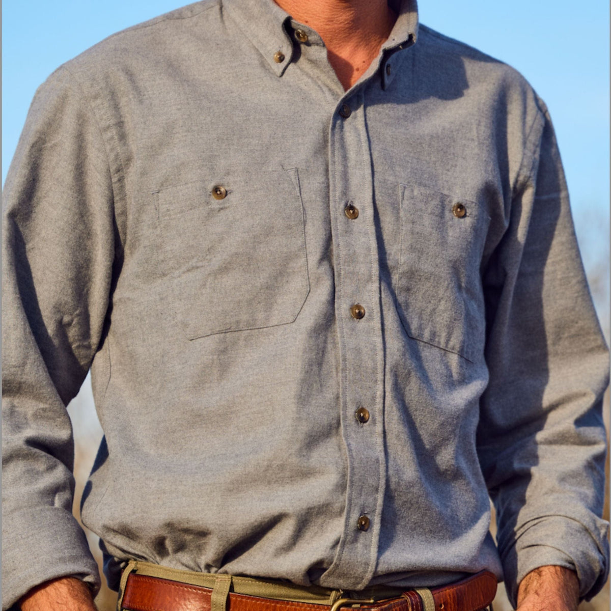 Man wearing Tom Beckbe Dixon Brushed Cotton Twill Shirt in light gray with two chest pockets and brown belt outdoors.
