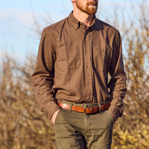 Man wears a brown Tom Beckbe Dixon Brushed Cotton Twill Shirt and olive green pants outdoors, hands in pockets.