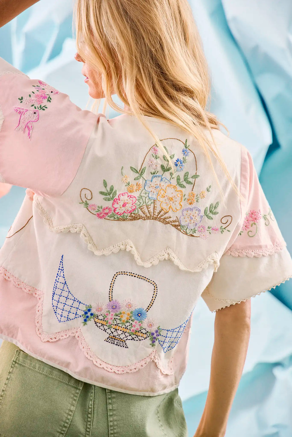 Back of the Bryce Top in Lazy Daisy paired with green Mallory Jeans in front of blue wall.