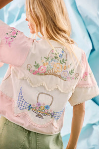 Back of the Bryce Top in Lazy Daisy paired with green Mallory Jeans in front of blue wall.