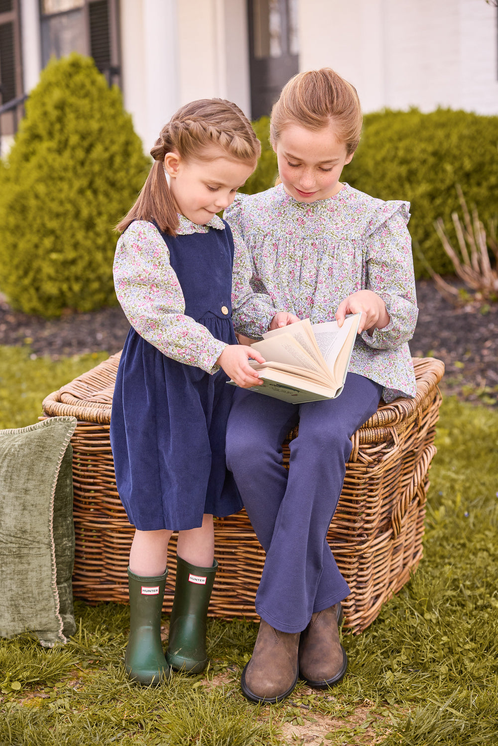 Two girls reading outdoors; younger in navy button-panel jumper and floral blouse, older in floral top and navy leggings