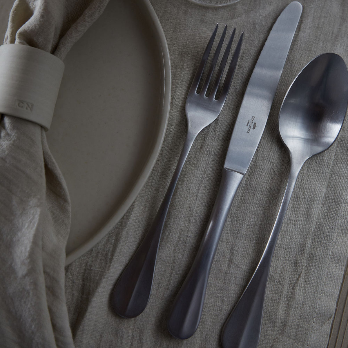 Overhead view of Nau Collection Flatware Set in Brushed, Set of 5 showcasing solid handles beside a plate on linen