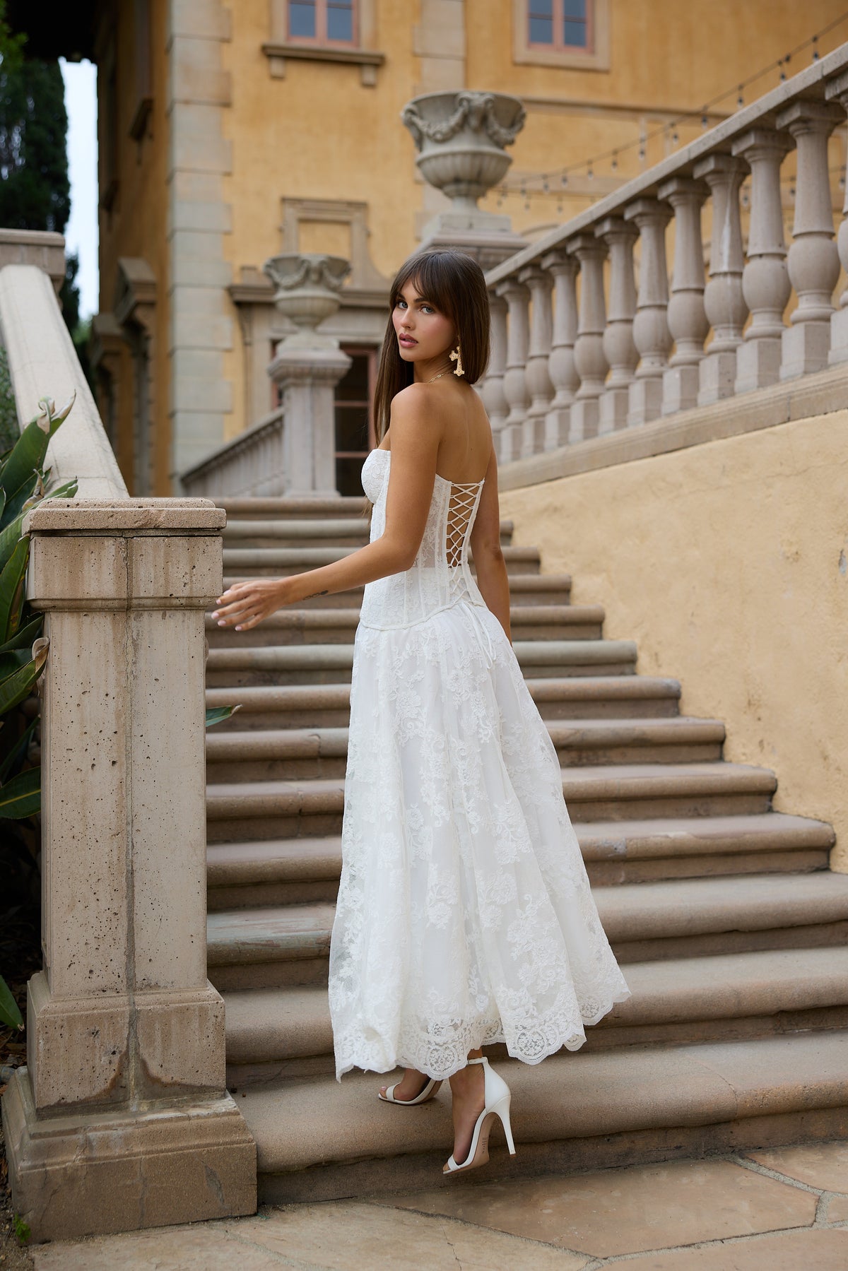 Rear view of The Carolena Set in White Chantilly Lace showcasing lace-up back and paisley embroidery on stone steps