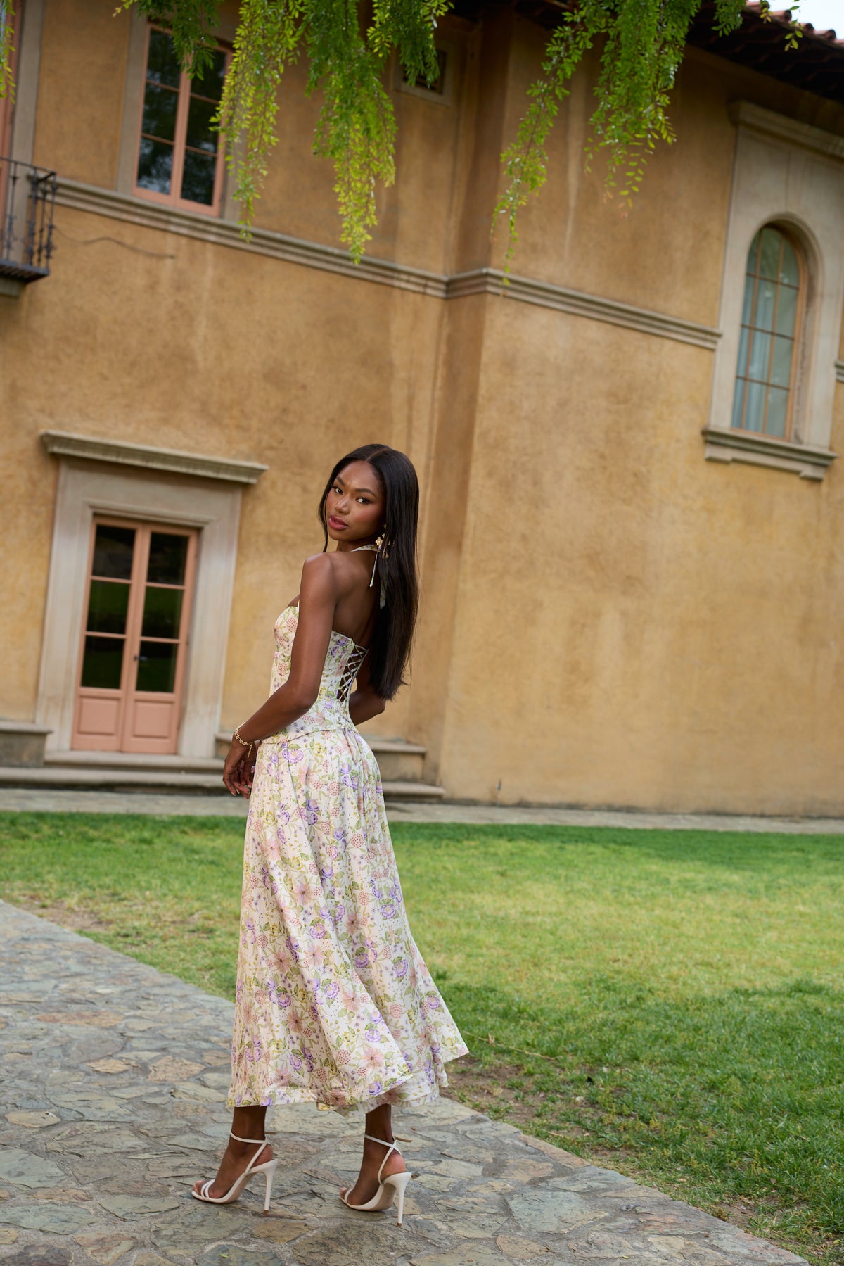 Back three-quarter view of The Carrie Set in Cordoba Print showcasing lace-up back and floral satin skirt outdoors