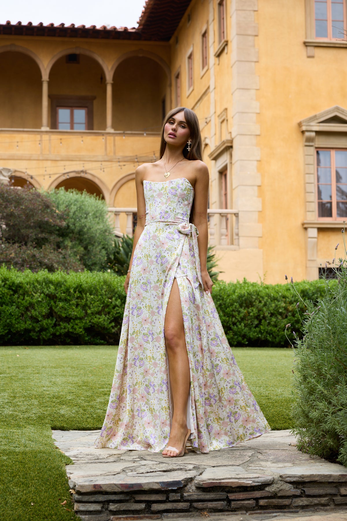 Front view of The Cecilia Dress in Cordoba Print showcasing floral satin, corset bodice, side slit and bow detail in a garden
