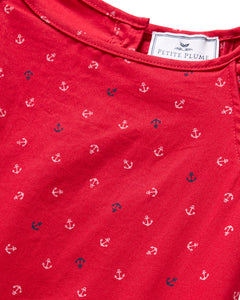 Close-up of a red fabric with small white and navy anchors, radiating nautical charm. The label reads Petite Plume, indicating the luxurious Girls Twill Amelie Nightgown in Anchors Away, crafted from lightweight woven cotton for ultimate comfort.
