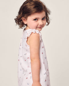 A young girl with short, curly brown hair gazes over her shoulder, wearing Petite Plumes Girls Twill Amelie Nightgown in Coastal Charms against a plain background.
