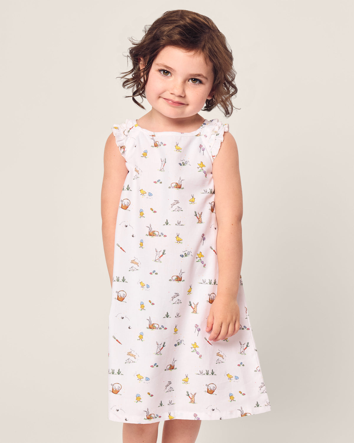 A young child with short brown hair wears the Petite Plume Girls Twill Amelie Nightgown in Easter Frolic, smiles warmly at the camera against a plain background.