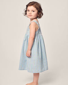 A young child with short, wavy brown hair stands barefoot against a light background. They are wearing Petite Plumes Girls Twill Charlotte Nightgown in Spring Gingham, looking slightly to the side.