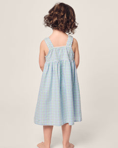 A young child with curly hair stands barefoot, facing away, wearing the Petite Plume Girls Twill Charlotte Nightgown in Spring Gingham against a plain light background.