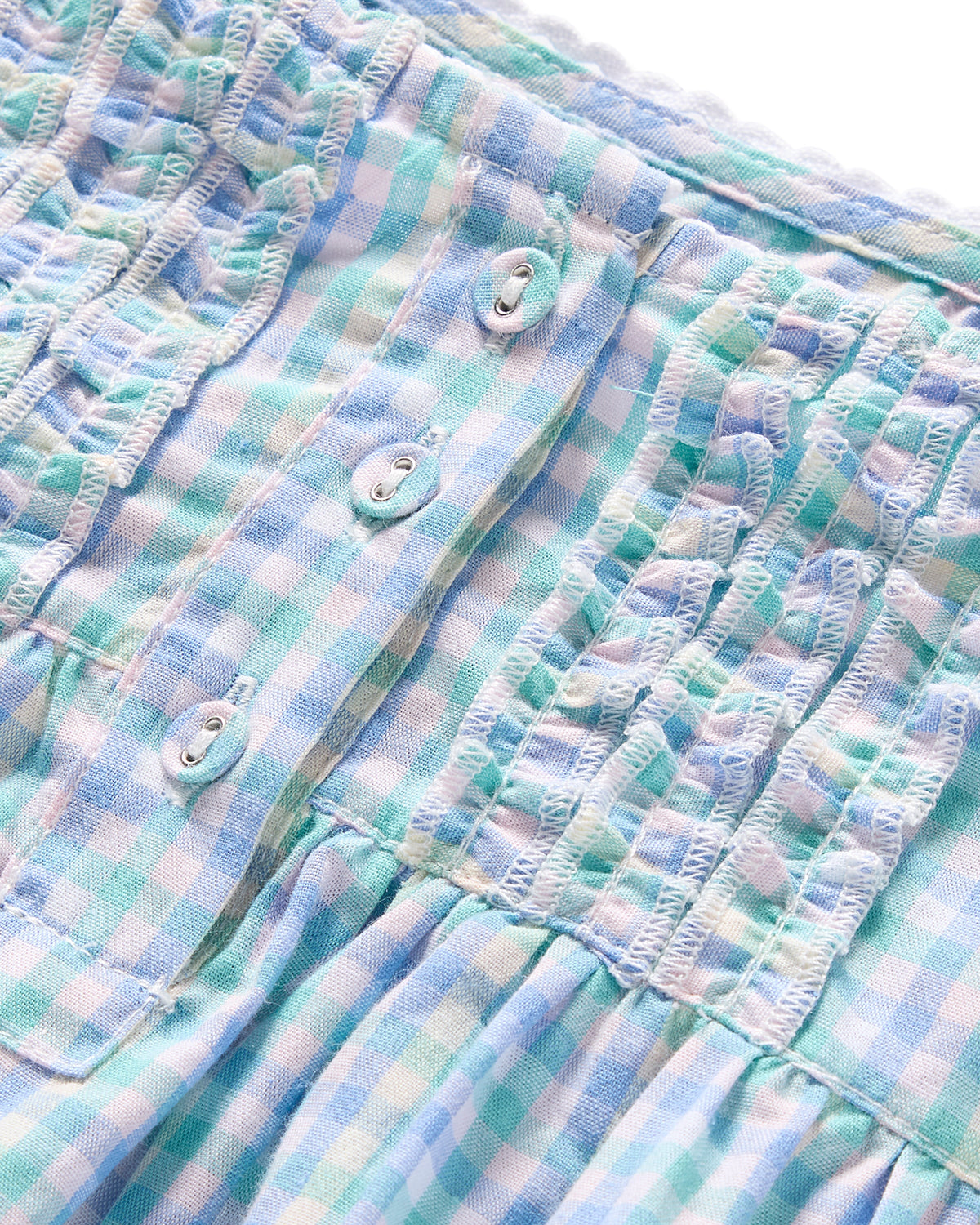 The Girls Twill Charlotte Nightgown in Spring Gingham by Petite Plume features a pastel blue and white gingham fabric with decorative ruffles and four buttons, giving it a textured, gathered appearance with its soft, lightweight design.