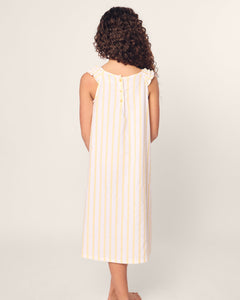 A person with long curly hair wears the Petite Plume Girls Twill Amelie Nightgown in Sunny Stripe, a sleeveless, ankle-length cotton dress with vertical yellow and white stripes, buttoned back, and ruffled shoulders. The background is plain off-white.