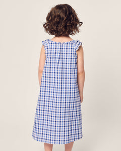 A young child with curly brown hair stands in Petite Plume’s Girls Twill Amelie Nightgown in royal blue gingham, against a plain background.
