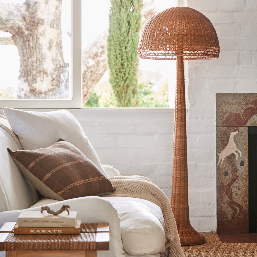 Right-side view of Augusta floor lamp showcasing woven rattan dome shade and tapered base beside a white sofa in a sunlit living room