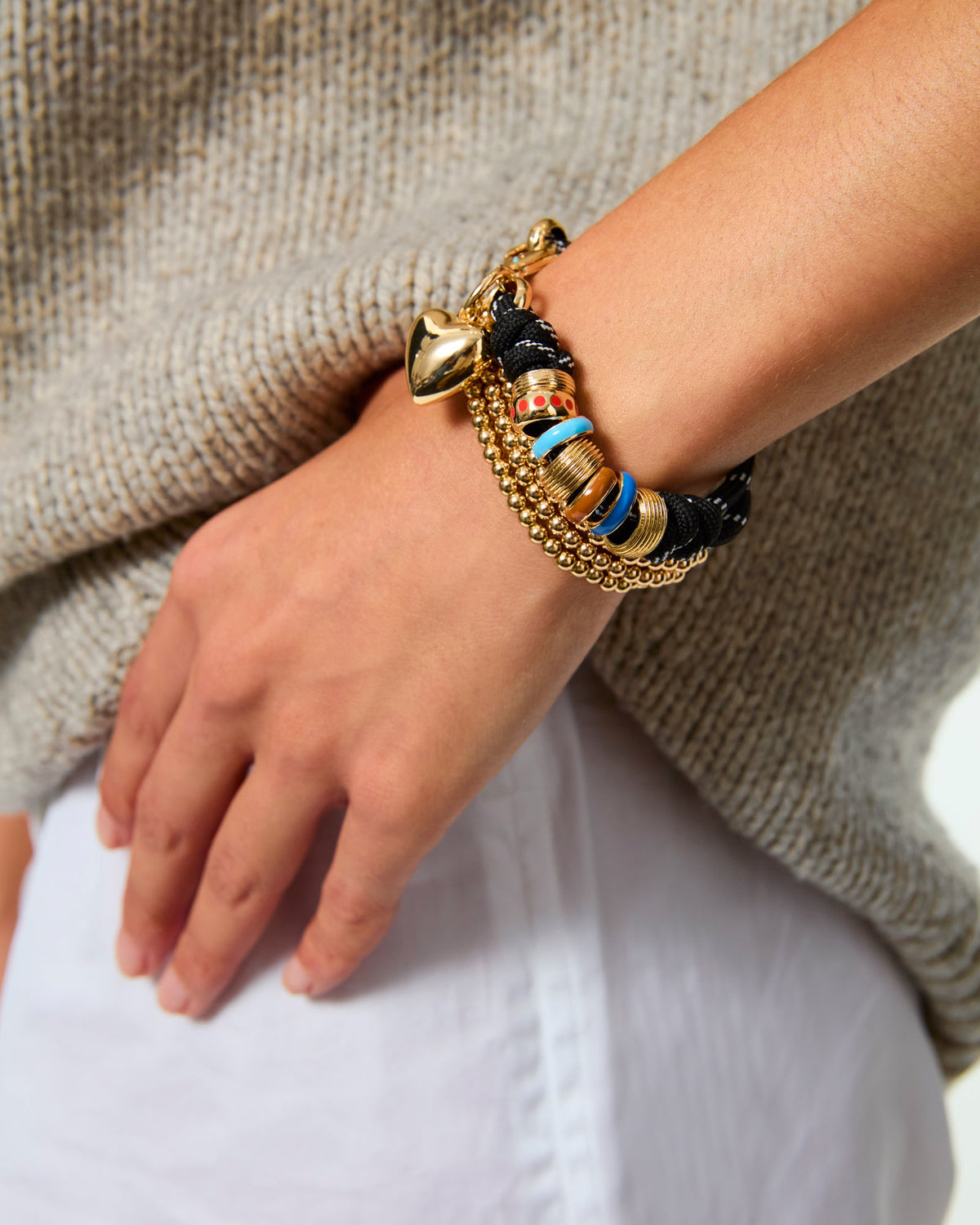 Close up of Super Size Happy Cord Bracelet on wrist with black cord, gold heart charm and colorful enamel sliders