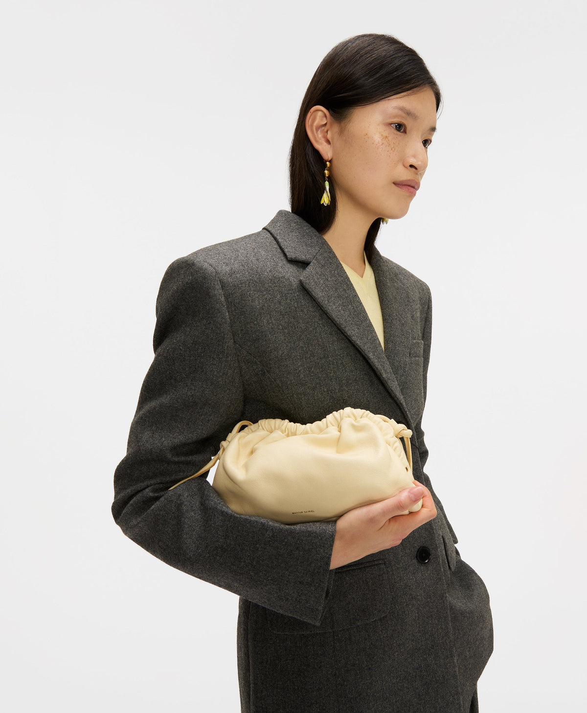 Side view of Mini Cloud Clutch in Jasmine showing ruched drawstring top and soft pouch shape held by model on white background