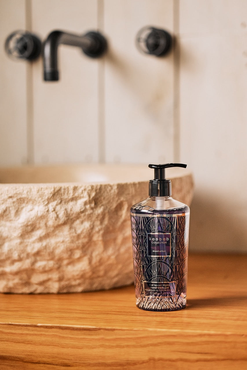 Baobab Collection Manhattan hand wash gel bottle sitting on a wooden vanity in front of a stone sink and wall-mounted faucet