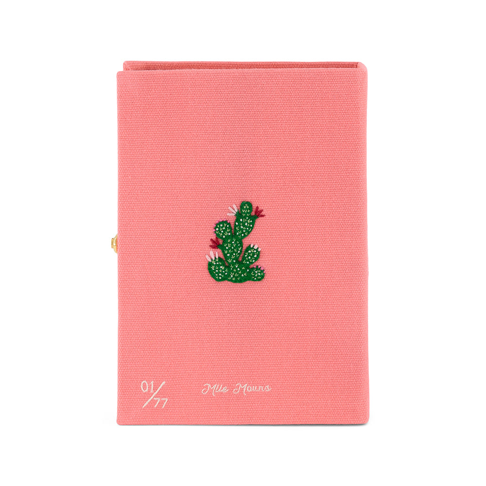 Front view of Wild and Free book clutch showing pink canvas cover with green embroidered cactus and handwritten “01/77” on white background