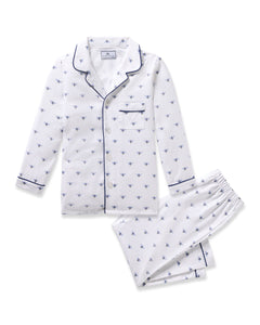 Petite Plumes Kids Twill Pajama in Buzzing Bees is a white cotton set with a long-sleeve button-up top and matching pants. Featuring navy blue trim on the collar, cuffs, and pocket, it is adorned with small blue buzzing bees for a charming contrast.