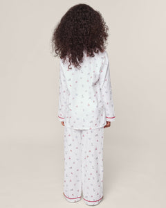 A child with curly hair, wearing a Petite Plume Kids Twill Pajama in Coastal Charms, featuring white yarn-dyed cotton and red and blue patterns, stands with their back to the camera against a plain background.