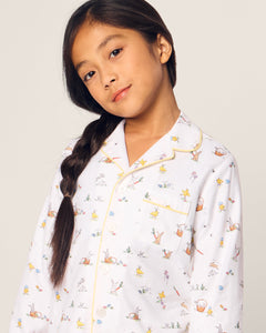 A young girl with long, dark hair in a side braid wears Petite Plumes Kids Twill Pajama in Easter Frolic. These flame retardant pajamas ensure her safety as she stands against a neutral background, looking at the camera with a slight smile.