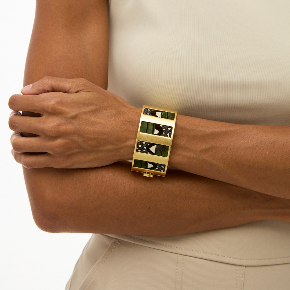 Close-up of Sage Striped Hinge Cuff showcasing gold hinged cuff with green and black feather inlays on model’s wrist against cream top