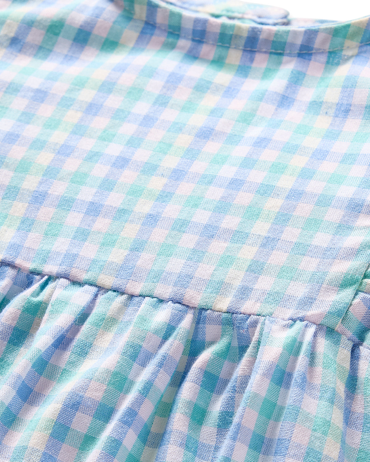 Close-up of Petite Plumes Babys Twill Ruffled Romper in Spring Gingham, featuring a gathered seam and a blue and green gingham pattern with small squares that evokes a soft, casual feel reminiscent of luxurious sleepwear.