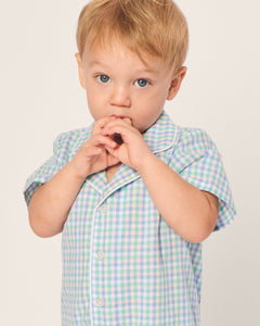 A toddler with light hair stands against a plain background, wearing Petite Plumes Babys Twill Romper in Spring Gingham, crafted from soft, yarn-dyed cotton. They have their hands near their mouth and are looking slightly upward.