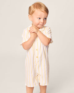 A toddler with light hair wears Petite Plumes Babys Twill Summer Romper in Sunny Stripe. They have a thoughtful expression, clasping their hands against a plain background.