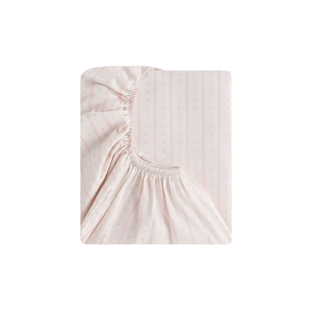 Folded view of Petal Scallops crib sheet in pink showcasing scallop-stripe pattern and elasticized fitted corner on white background
