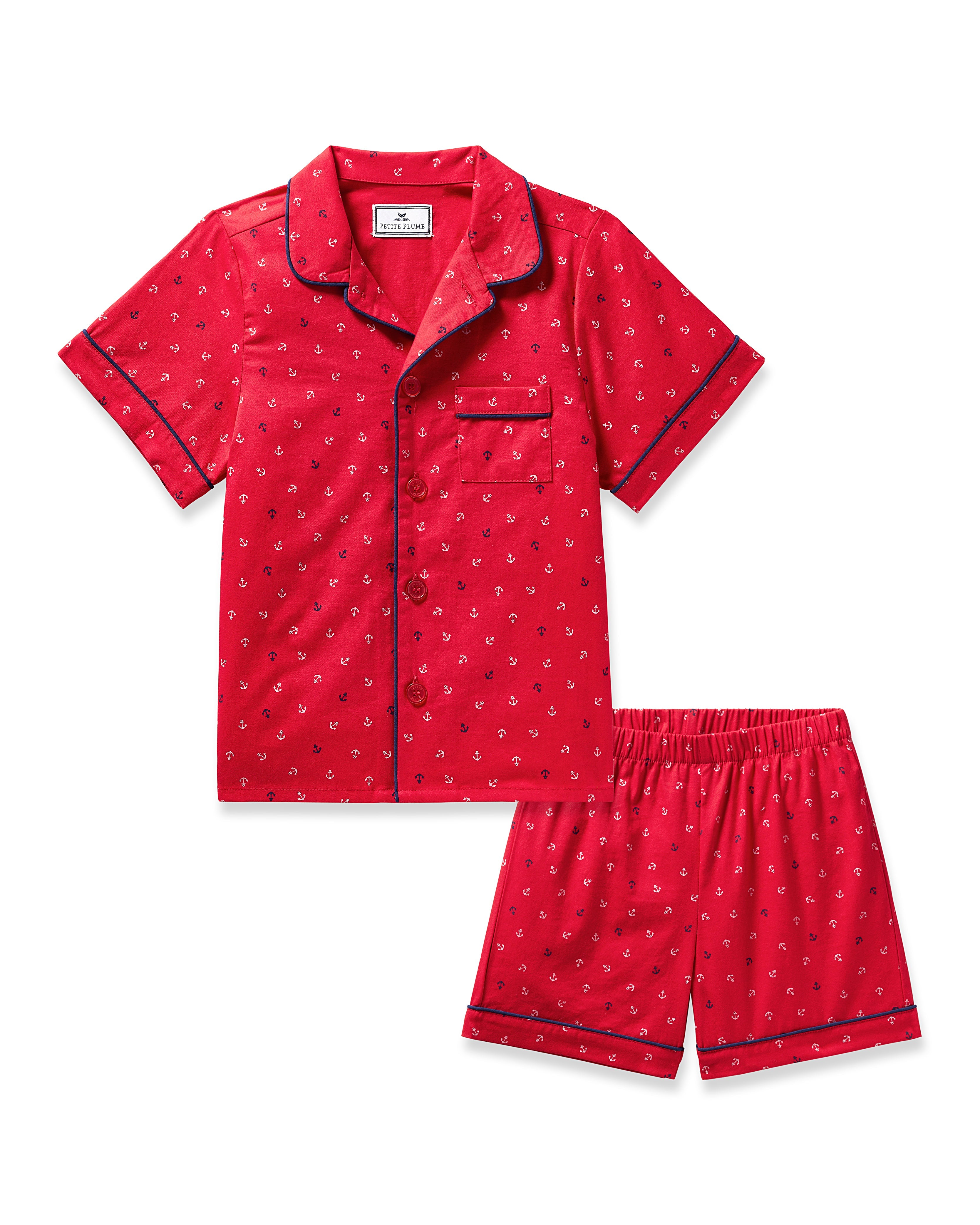 The Kids Twill Short Set in Anchors Away by Petite Plume features luxurious red pajamas with a small anchor pattern. The collared, button-up top has black piping and a chest pocket, while the matching shorts have an elastic waistband. Made from flame-retardant fiber for safe, comfortable nights.