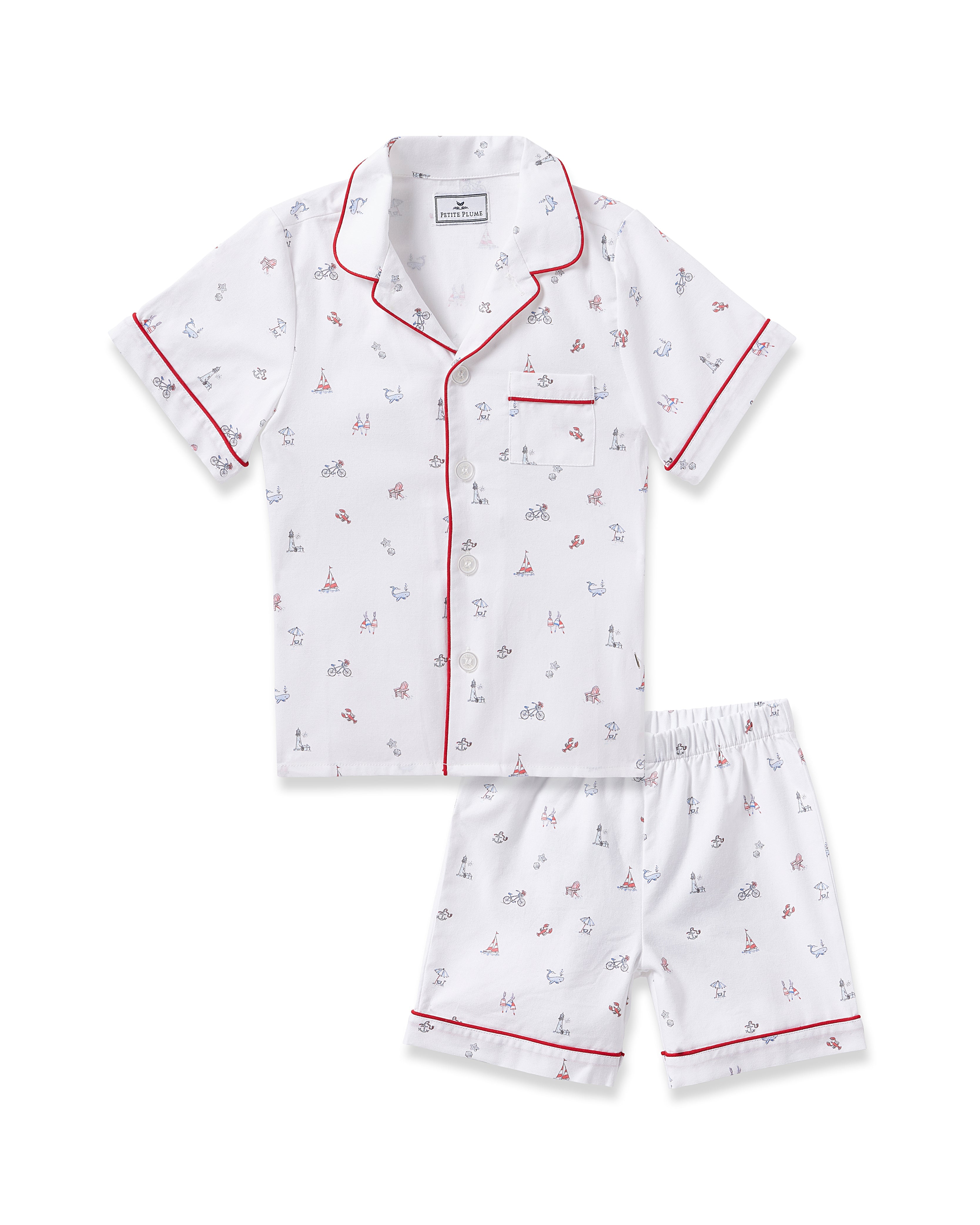 The Kids Twill Short Sleeve Short Set in Coastal Charms by Petite Plume offers white pajamas adorned with sails, anchors, and bicycles. Featuring red piping and a chest pocket, these stylish pieces offer both luxury and flame retardant safety.