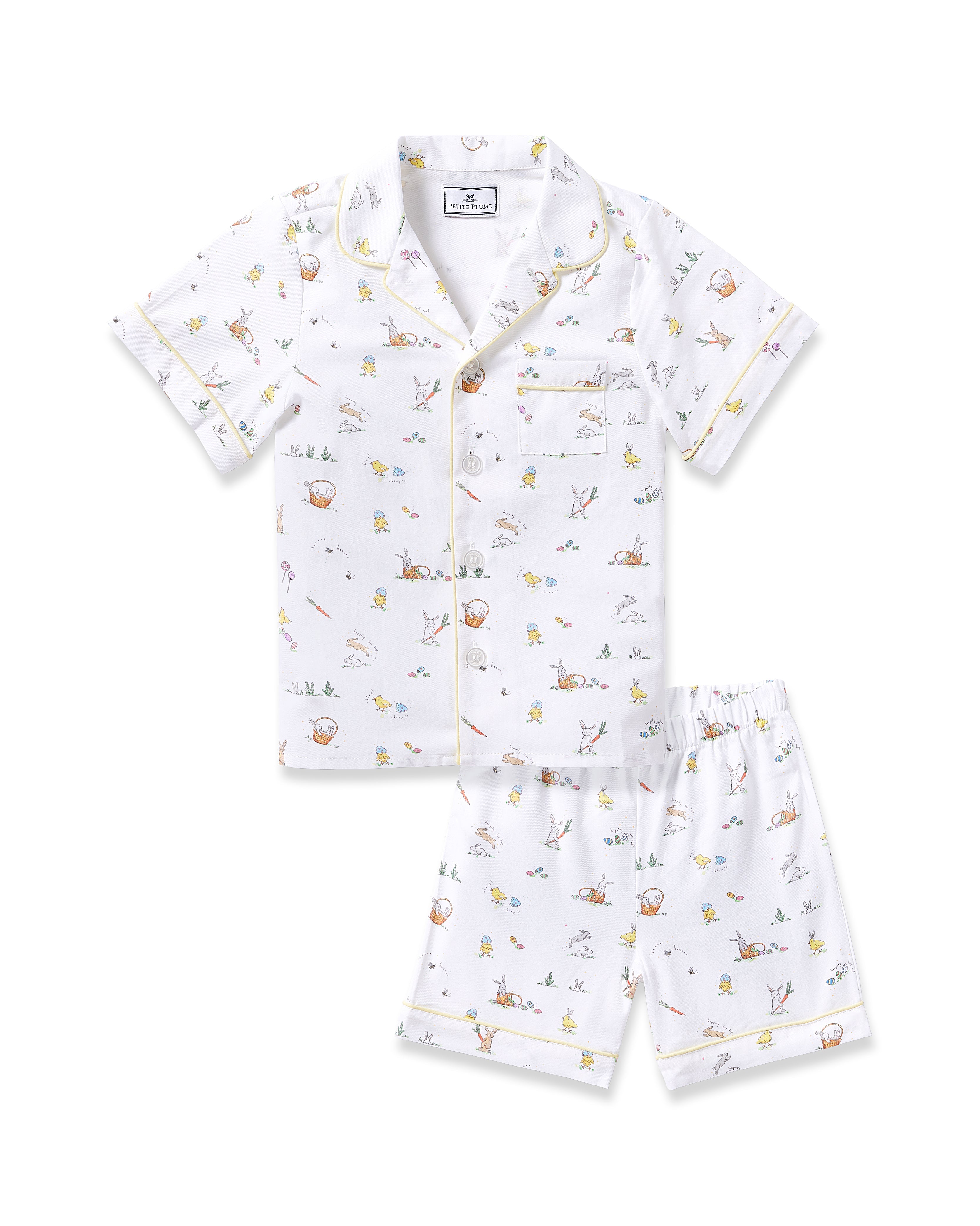 The Kids Twill Short Set in Easter Frolic by Petite Plume is a classic white pajama ensemble featuring short sleeves and shorts with multicolored animal and nature prints. The top has a collar, buttons, and a small pocket on the left.