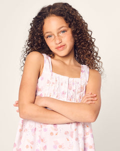 A curly-haired girl wearing Petite Plumes Girls Twill Charlotte Short Set in Seashell Splendor crosses her arms and smiles slightly against a plain background.
