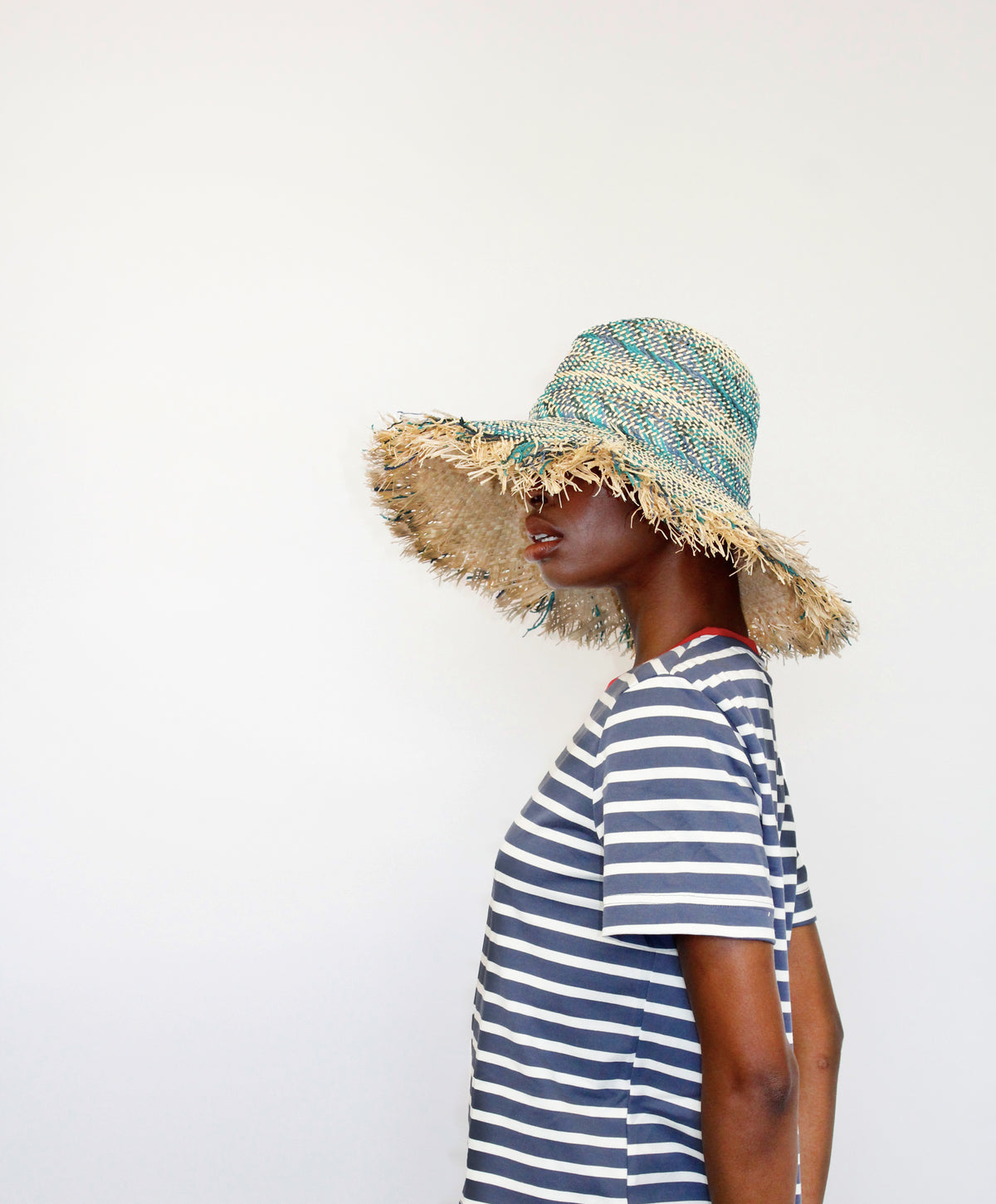 Side view of Cadence Hat in Bathroom Blue showcasing its turquoise and neutral woven fedora shape with fringed brim on a model
