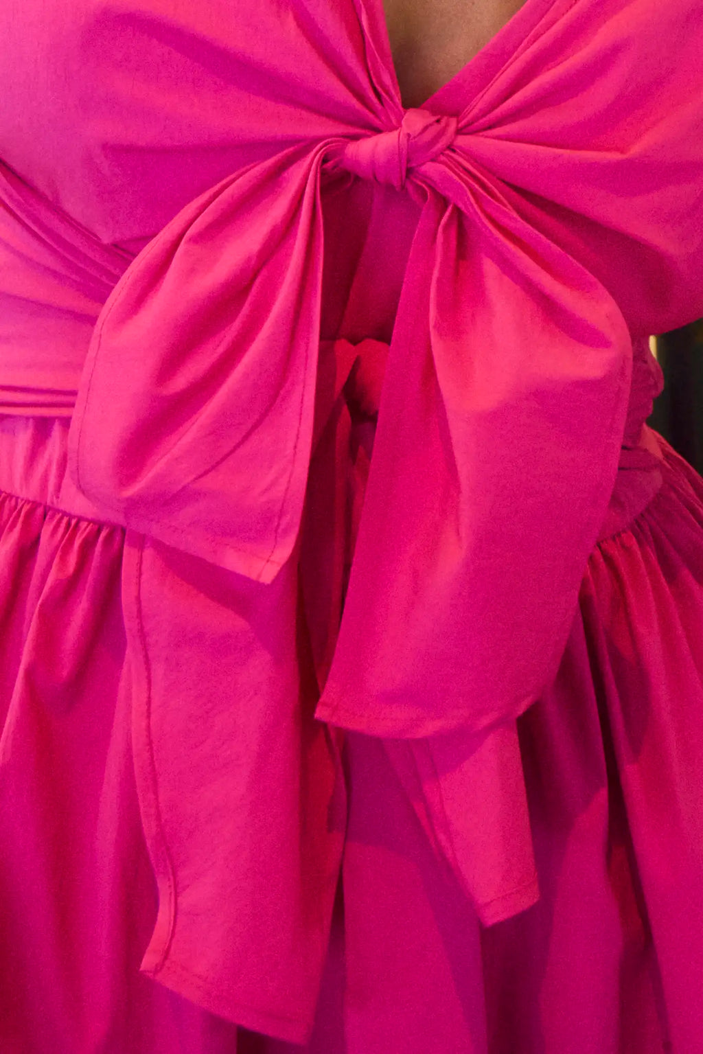 The Calista Dress in bright fuchsia has a tie-front bodice and full skirt.